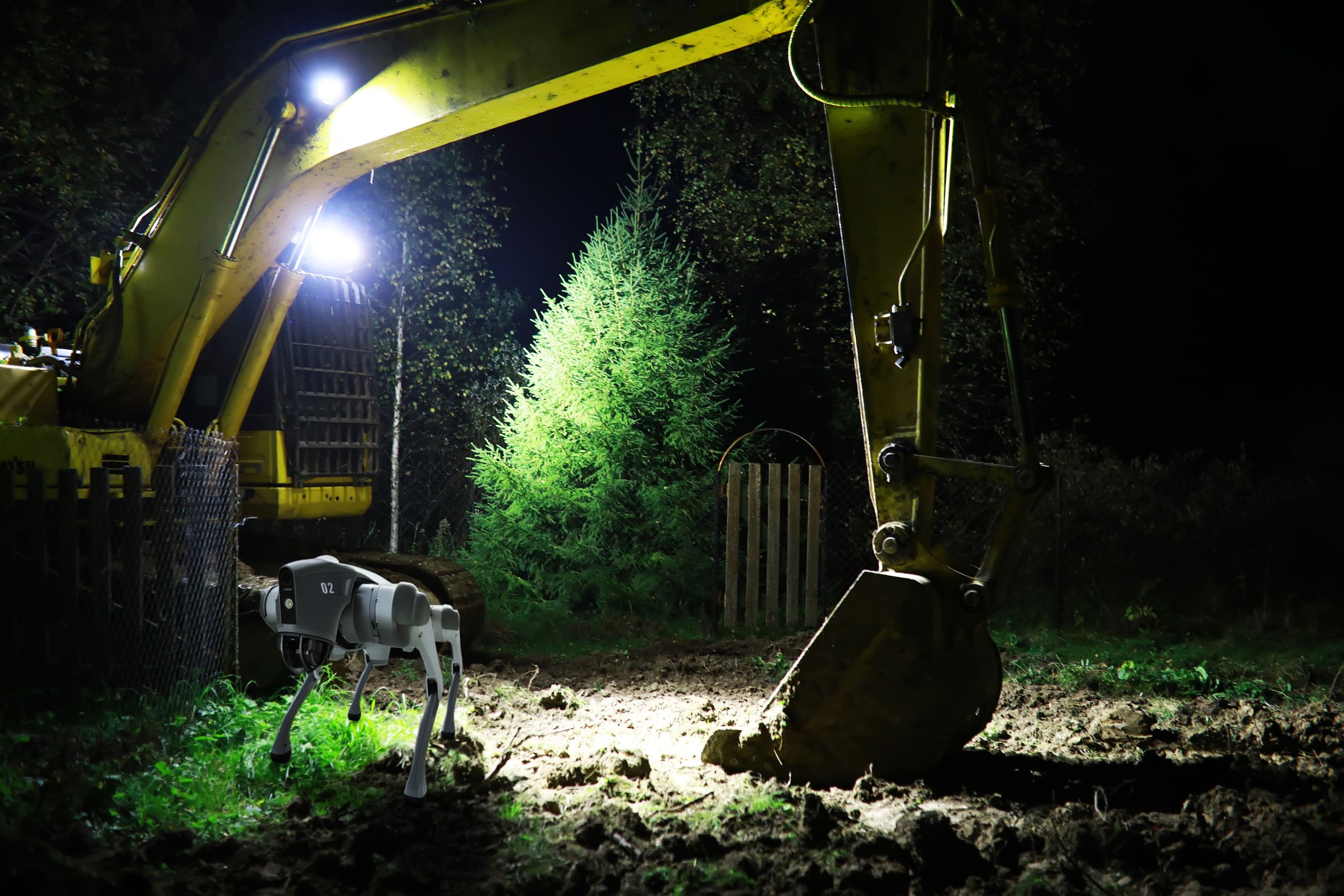 Excavator Illuminated at Night Working on Construction Site Near Lush Green Tree